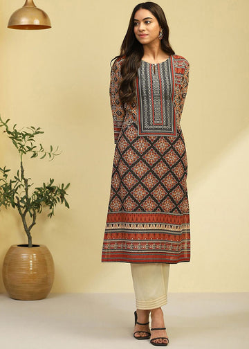 A woman modeling a long-sleeved kurta with a geometric and floral print in red, black, and beige, paired with cream pants and black sandals, set against a warm beige background with a potted plant.
